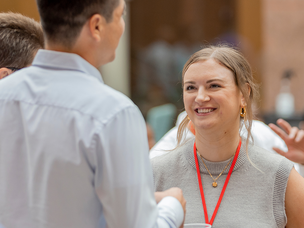 A woman wear a red lanyard and smiles talking to a man.