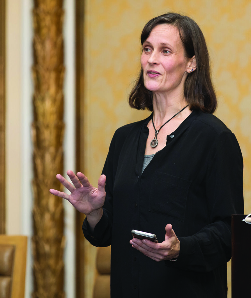 A professor speaks while holding a smartphone in her hand.