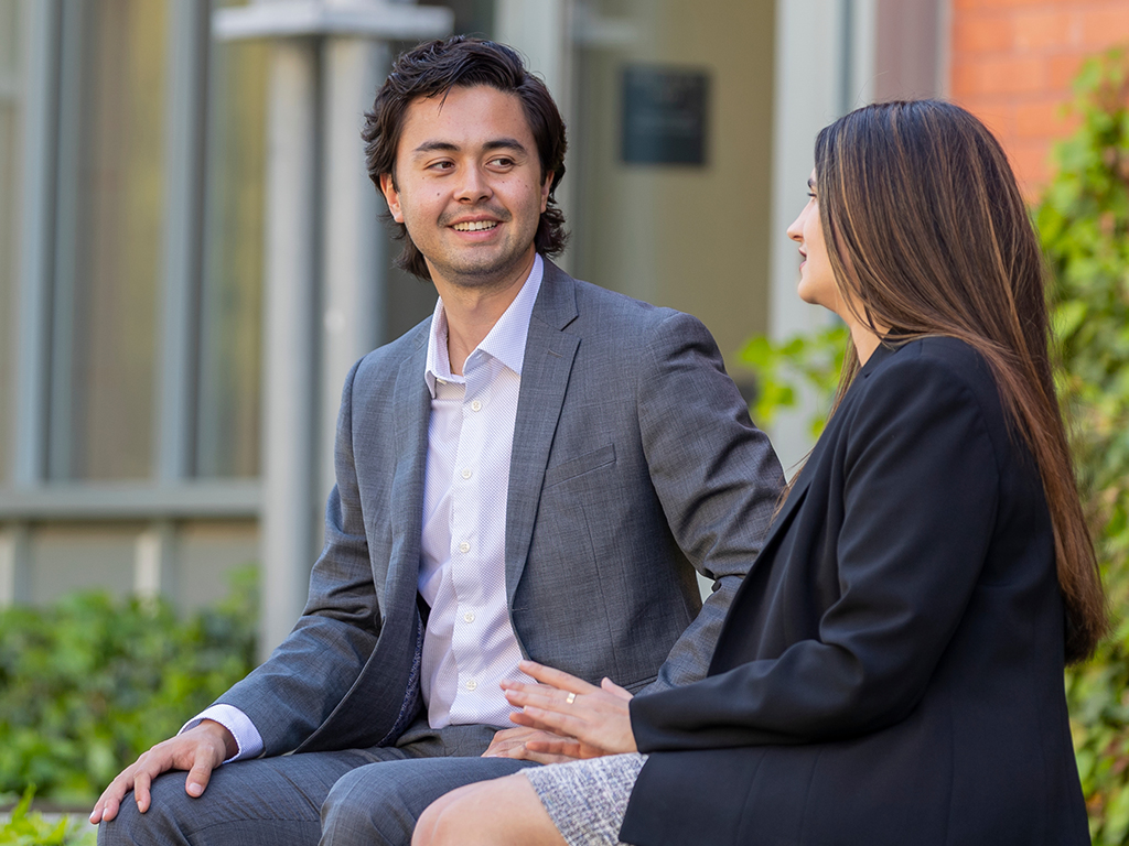 Two people in business attire sit outside talking.