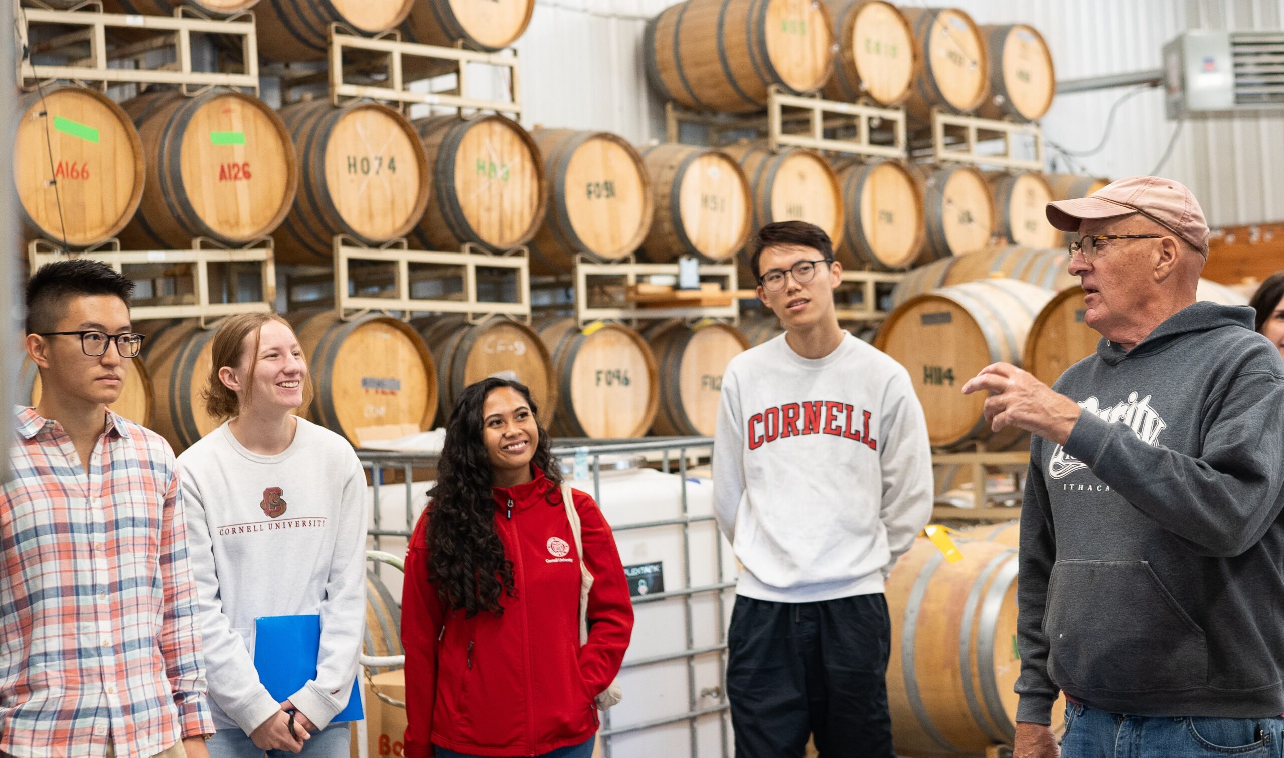 Four students and the owner of Treleaven winery stand in front of wooden wine barrels.