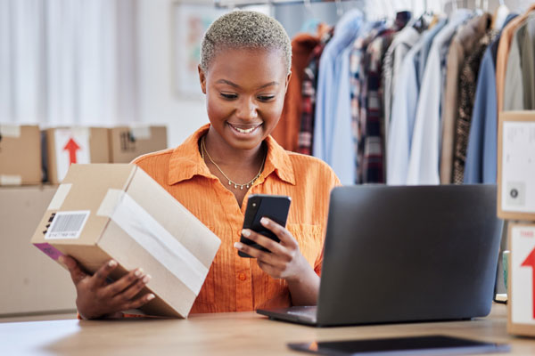 A woman smiles at a phone while holding a package.