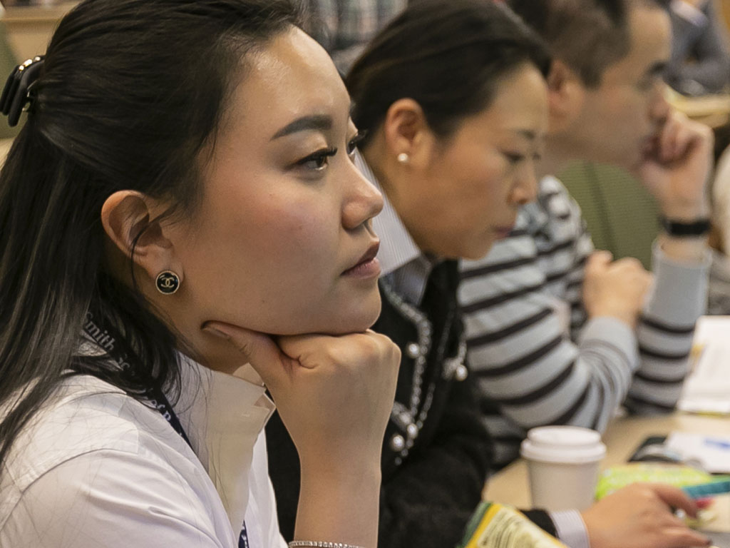 A woman sits at a table looking forward with her chin resting on her fist.