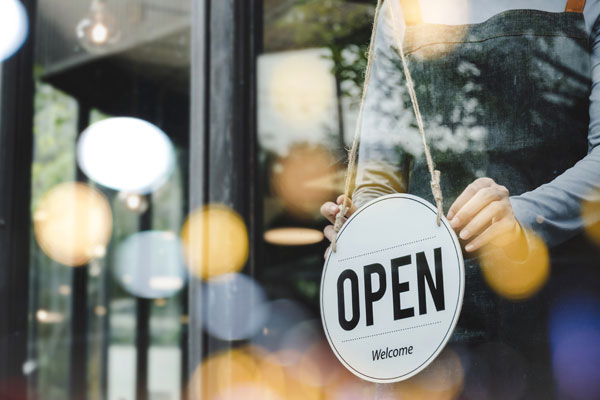 A person flips an “open” sign in a storefront window.