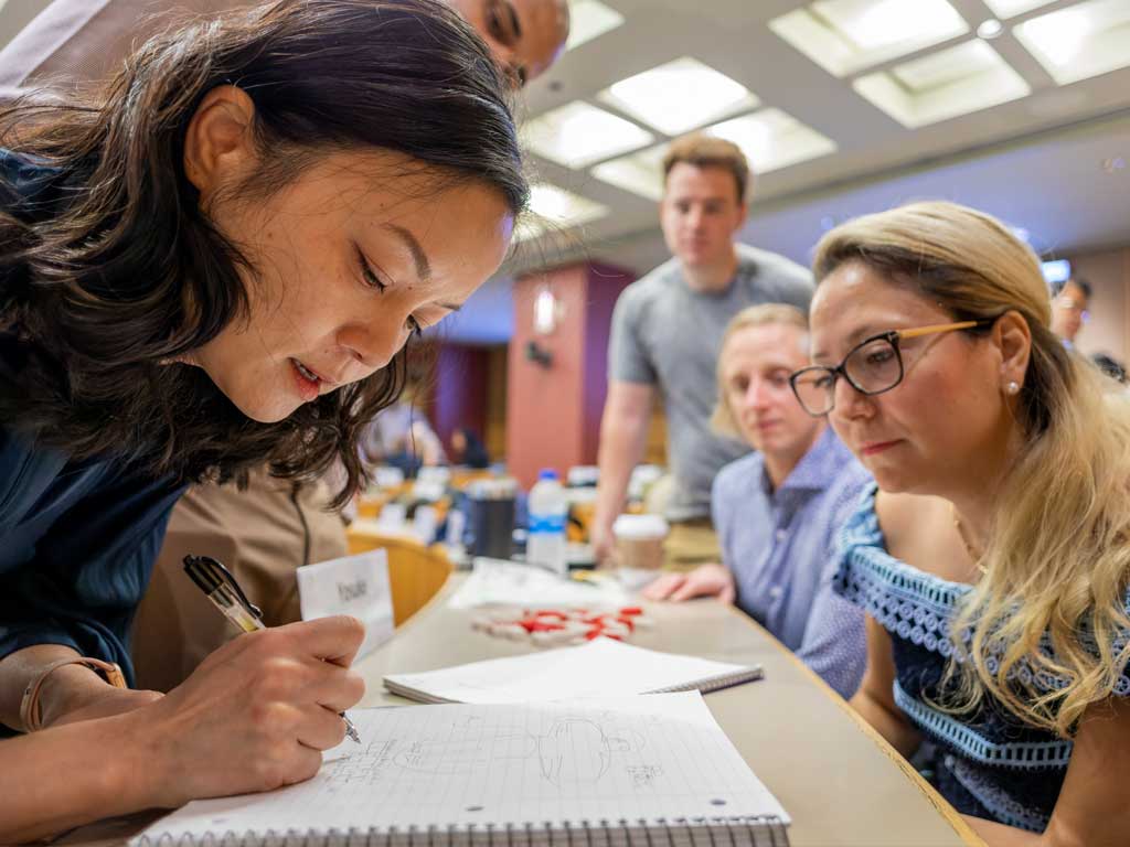 A woman writes with a pen in a notebook while other people look on.