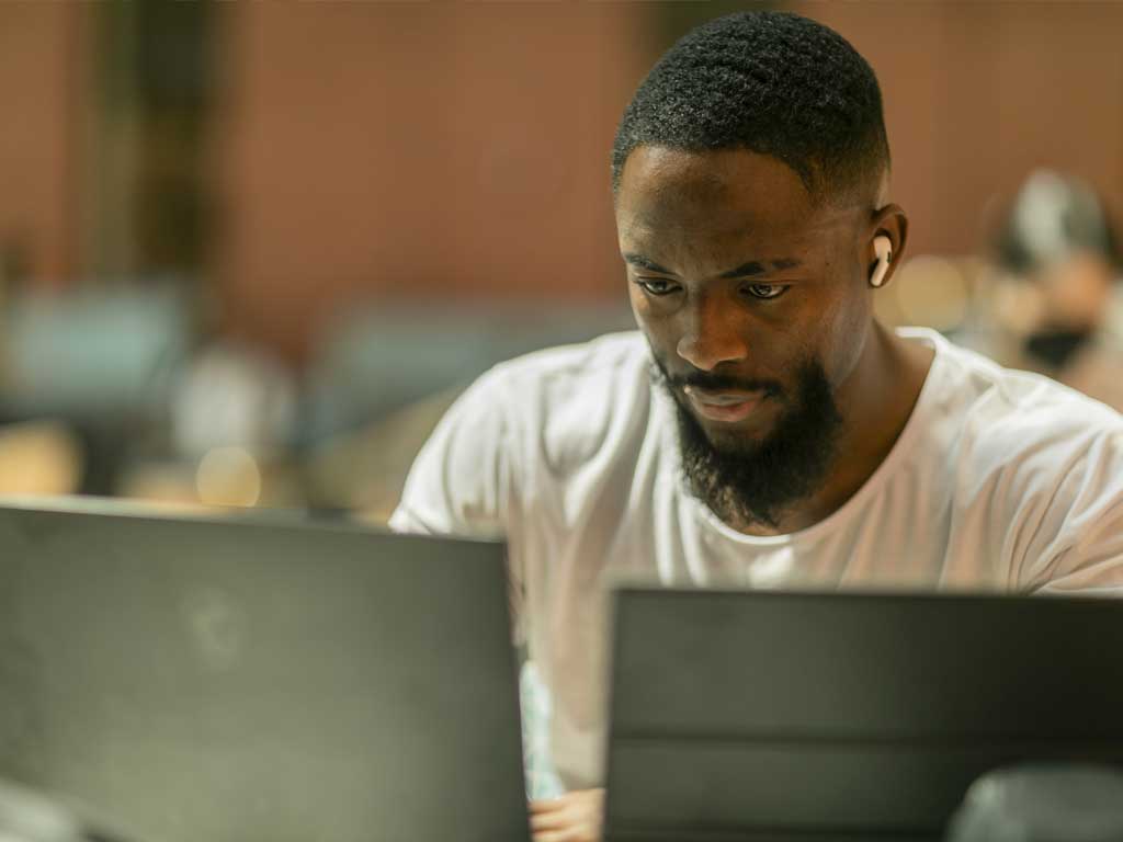 A man wearing earbuds types on a laptop.