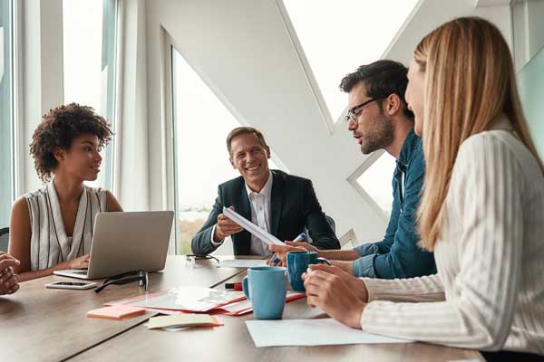 Four people sitting around a conference table with laptops and coffee cups in front of them.