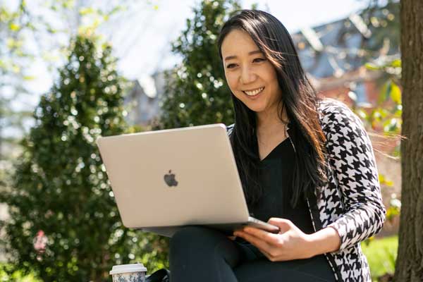 A woman sits outside with a laptop.