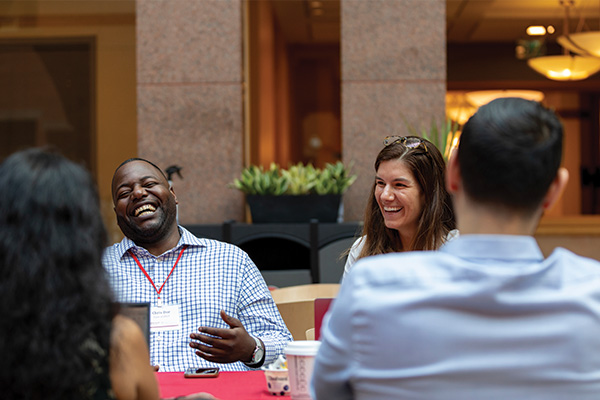 A small group of people talking and laughing at a table in the Sage Hall atrium.