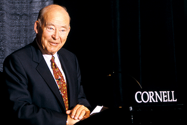 Samuel Curtis Johnson Jr. in a suit and tie standing at a podium that says “Cornell.”