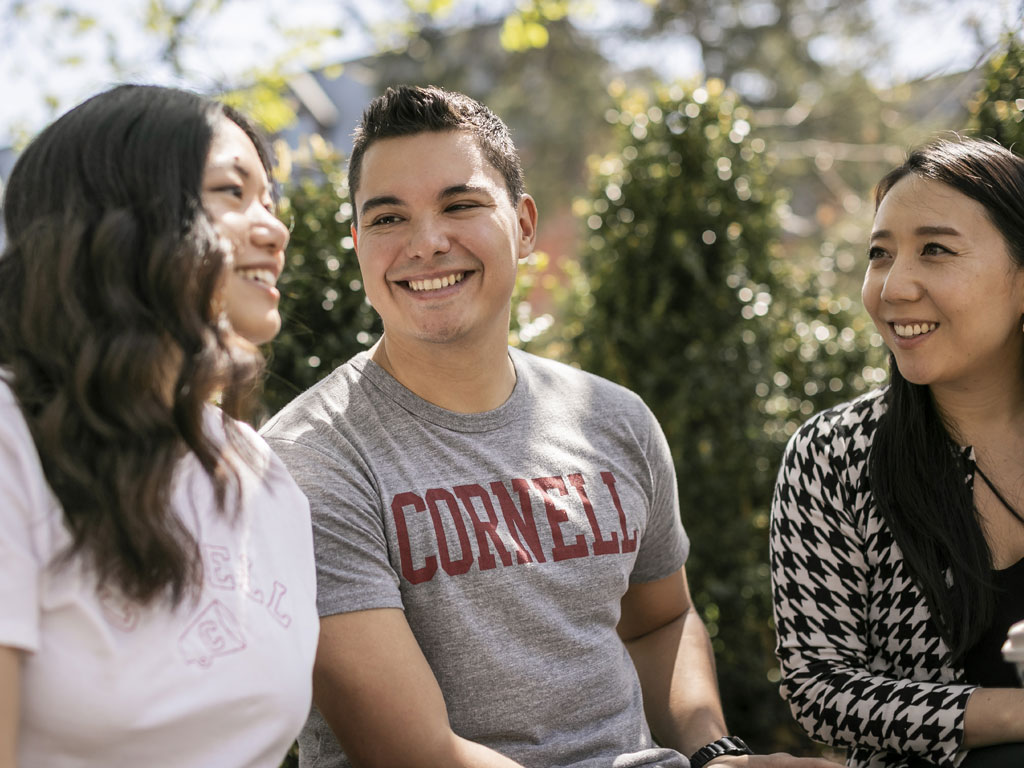 Three students sitting outside smiling.
