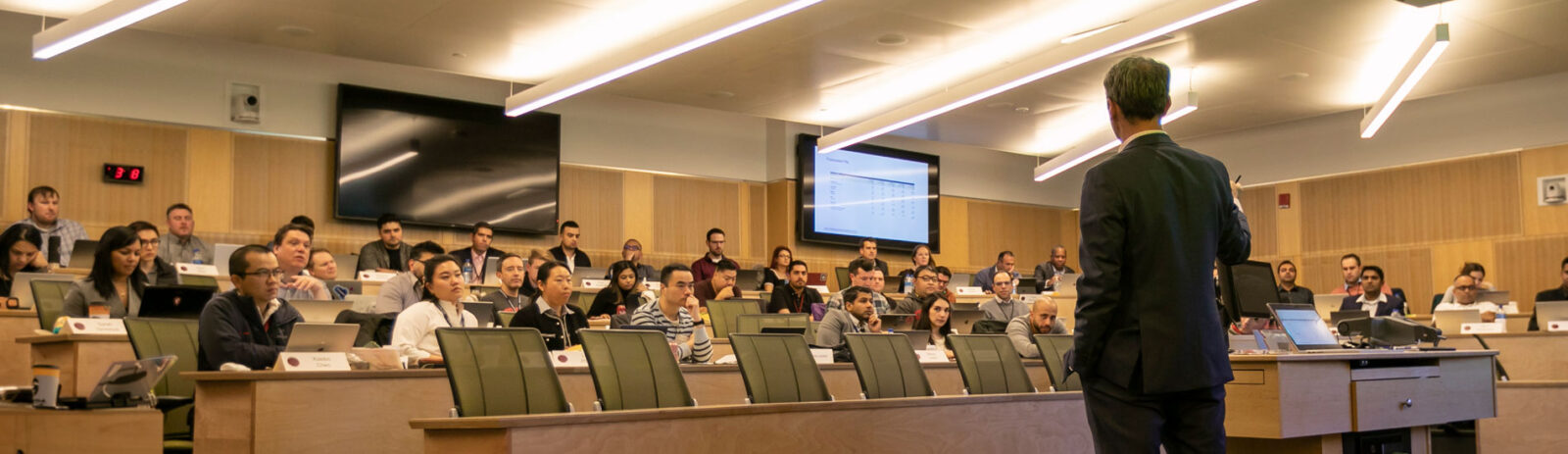 Person in a suit stands in front of a tiered classroom