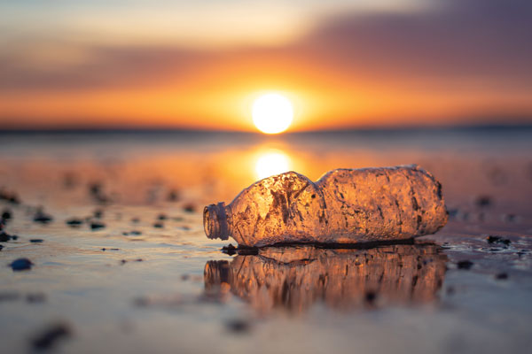 An empty plastic water bottle on a beach with the sun setting in the background.