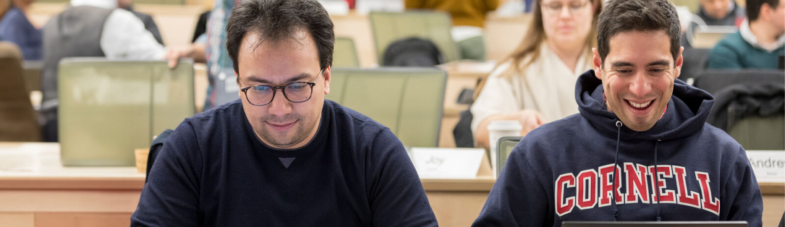 Two men sit in a tiered classroom.