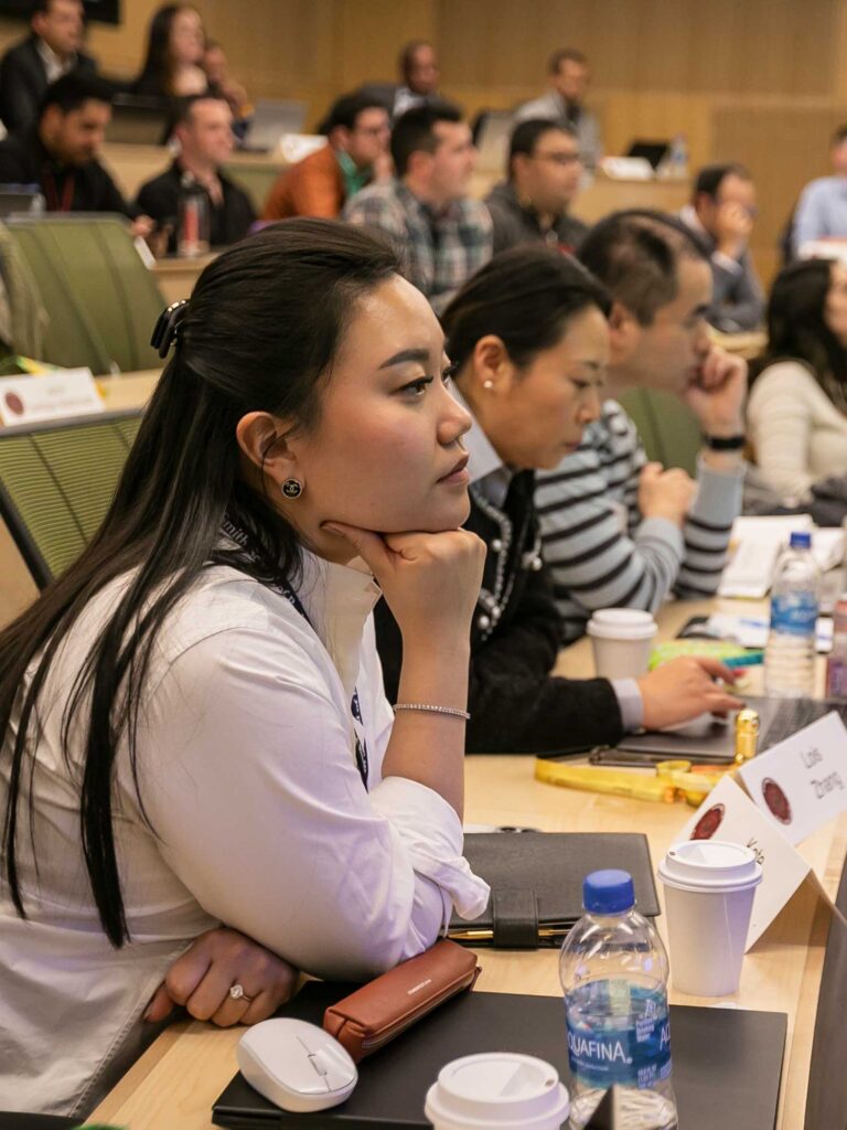 A woman sits in a tiered classroom with her chin resting on her fist.