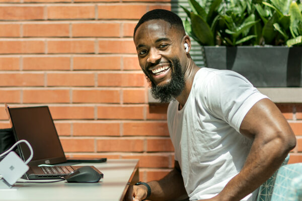 A male student smiling at the camera with his laptop in front of him.