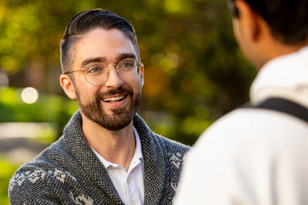A male student wearing glasses talking to another student.