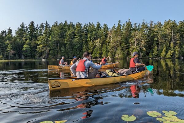Students in a canoe in water with trees in the background.