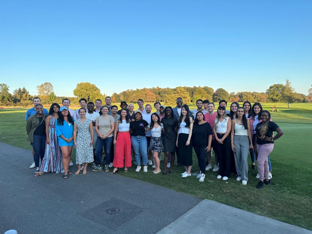 A large group of students pose for a photo outside in fall