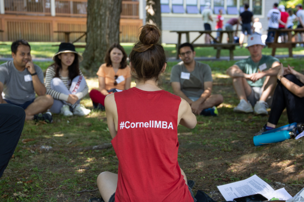 Students debrief while sitting in a circle outside on the grass.