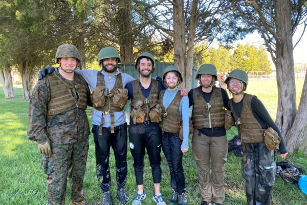 Students in camo protective gear stand together smiling for the camera.