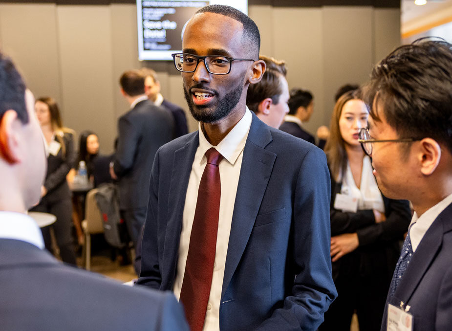 A man in business attire speaks in a circle of people.