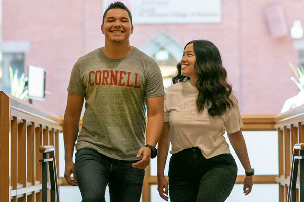 Two students in Cornell University t-shirts walk inside the Sage Hall atrium.