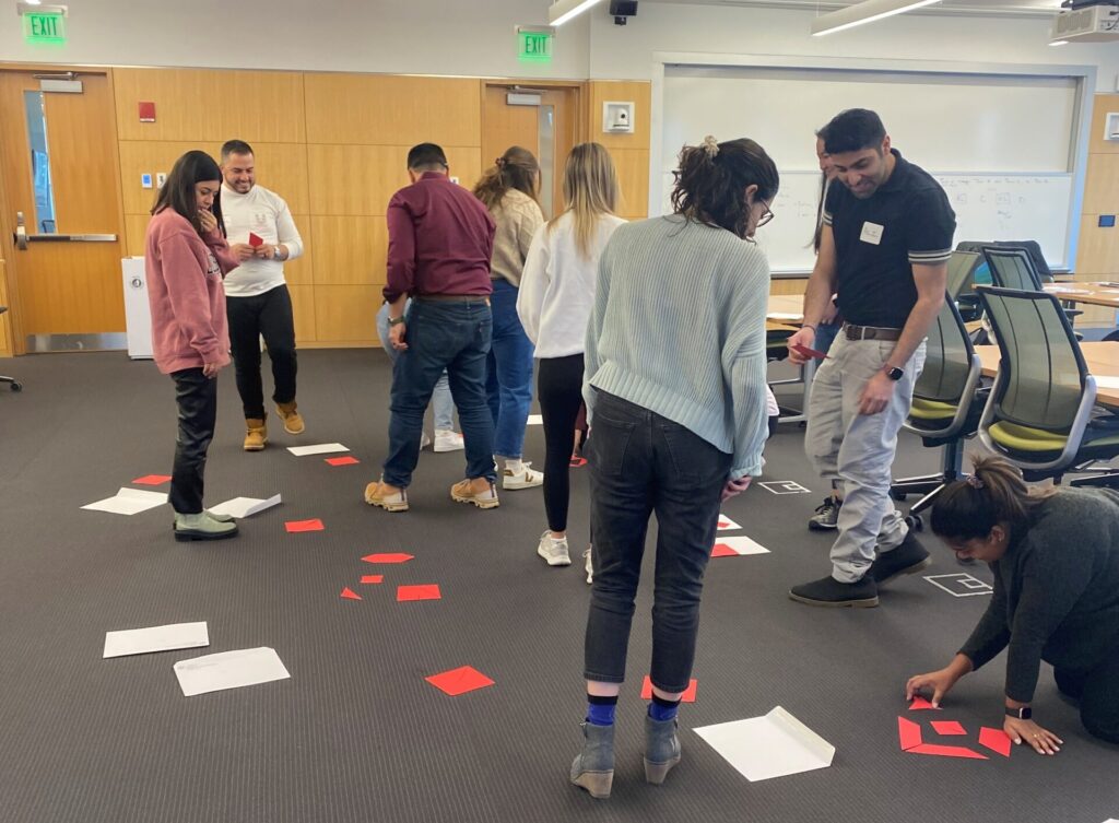 Students walk around a room looking at papers on the floor.