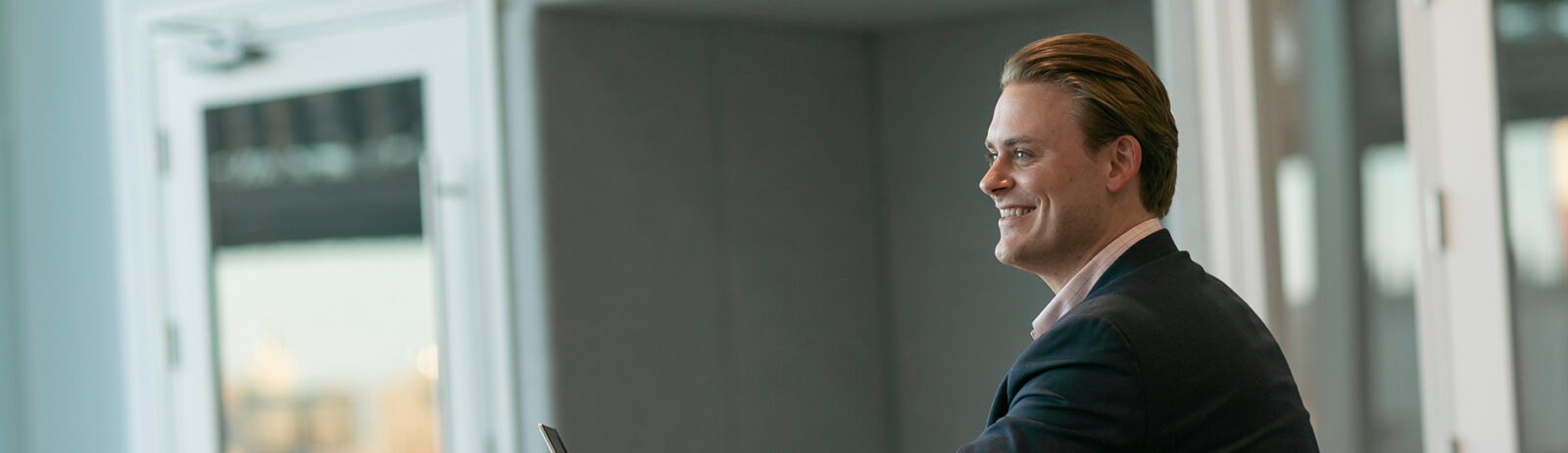 A man in a suit smiles as he sits at a table.