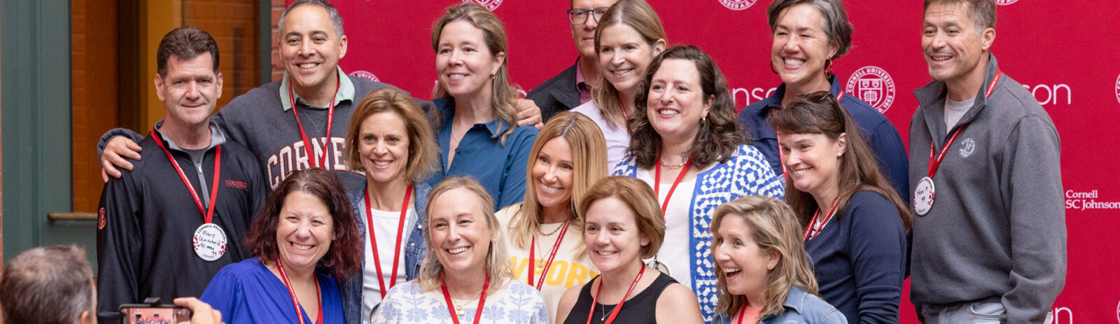 Alumni stand and smile in front of a red Johnson School banner.