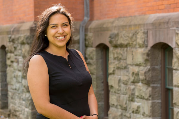 A woman in a black top stands in front of Sage Hall.