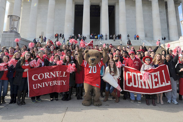 People and the Cornell mascot, the Big Red Bear, standing in front of the Lincoln Memorial with Cornell banners.