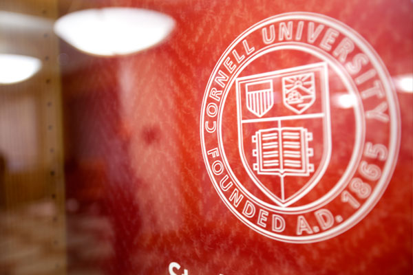 A white Cornell University seal on a red wall.