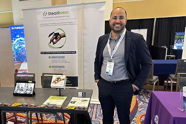 A man standing next to a table and a poster displaying information about Steadiwear.