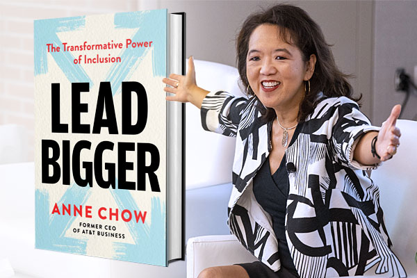 A woman in a black and white blazer with her hands outstretched to the right of an enlarged image of the book she authored.