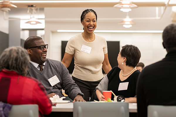 One person standing in front of a group of people sitting at a table.