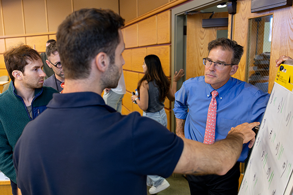 Two students stand and talk with a professor.