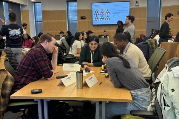 students sit at tables in a classroom working together on a class activity
