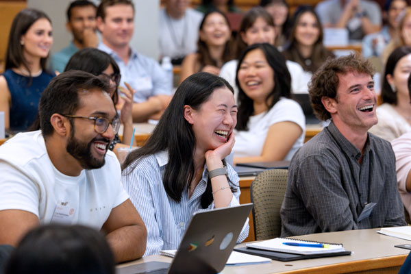 Students smiling and laughing in a tiered lecture hall setting.